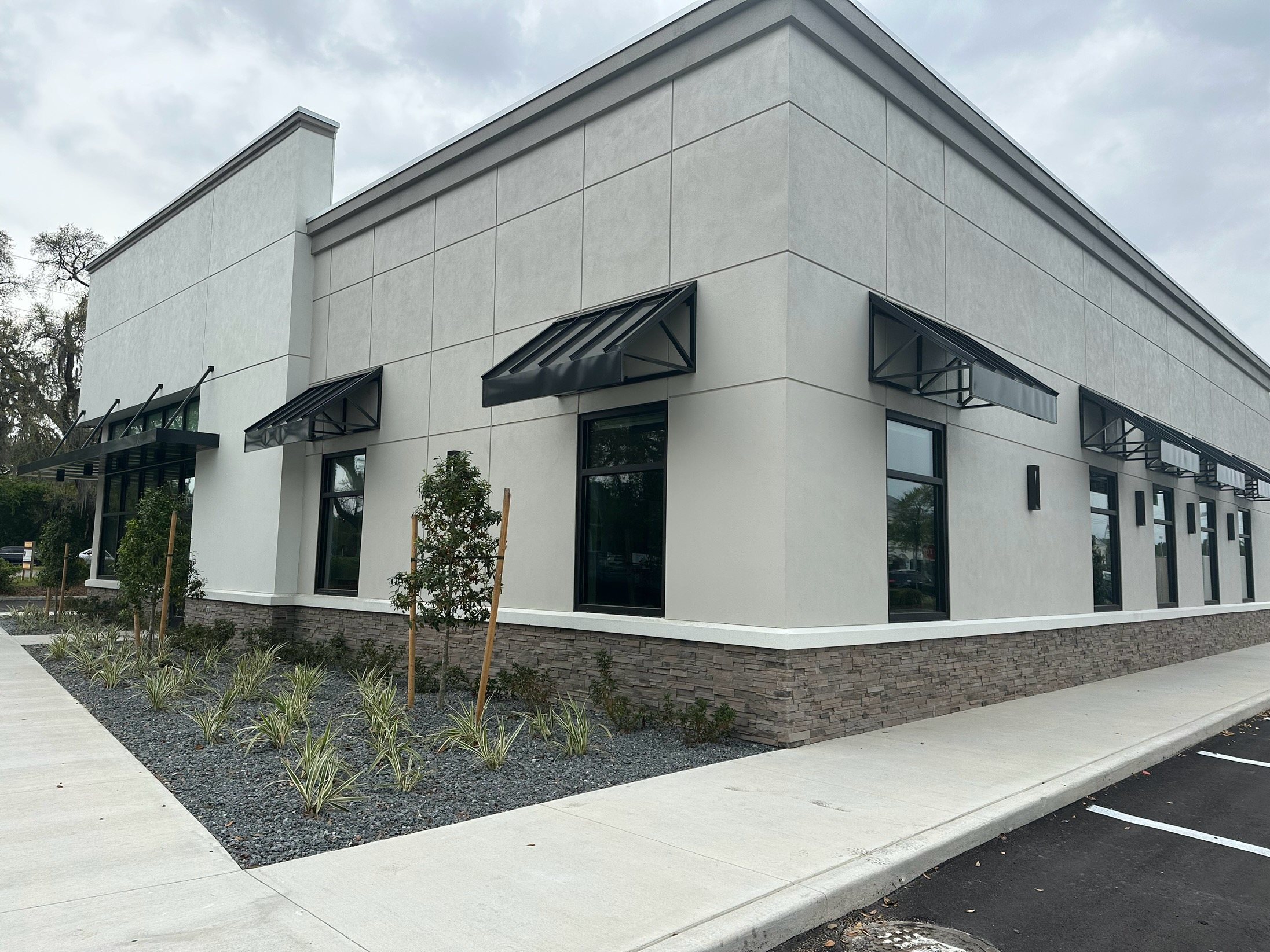 Black commercial awnings installed around a modern corner building